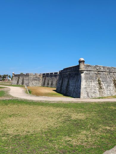 Stone fort wall under a clear blue sky, with grassy foreground and a dirt path.