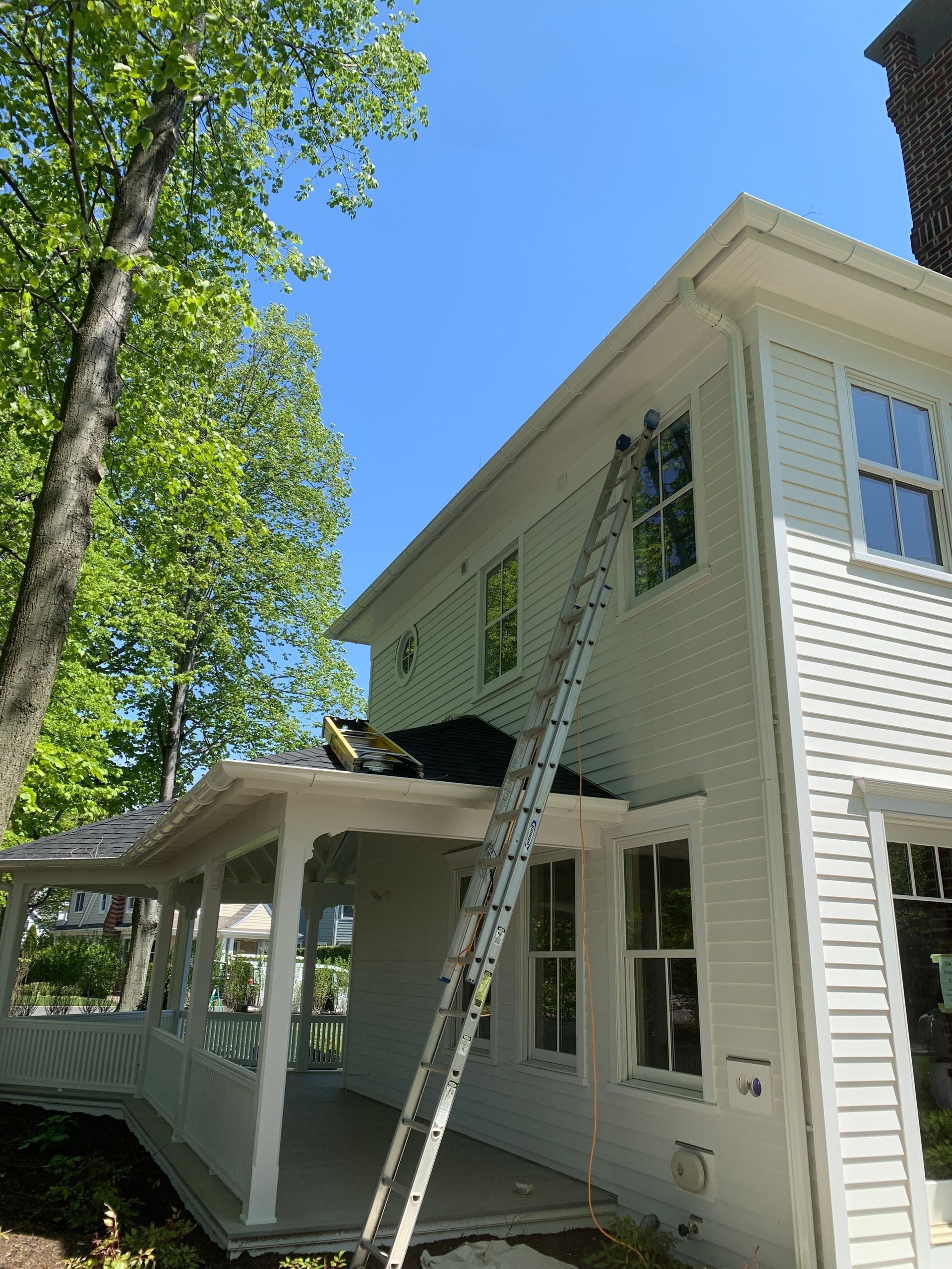White two-story house with a porch and a ladder reaching an upper window under a bright blue sky