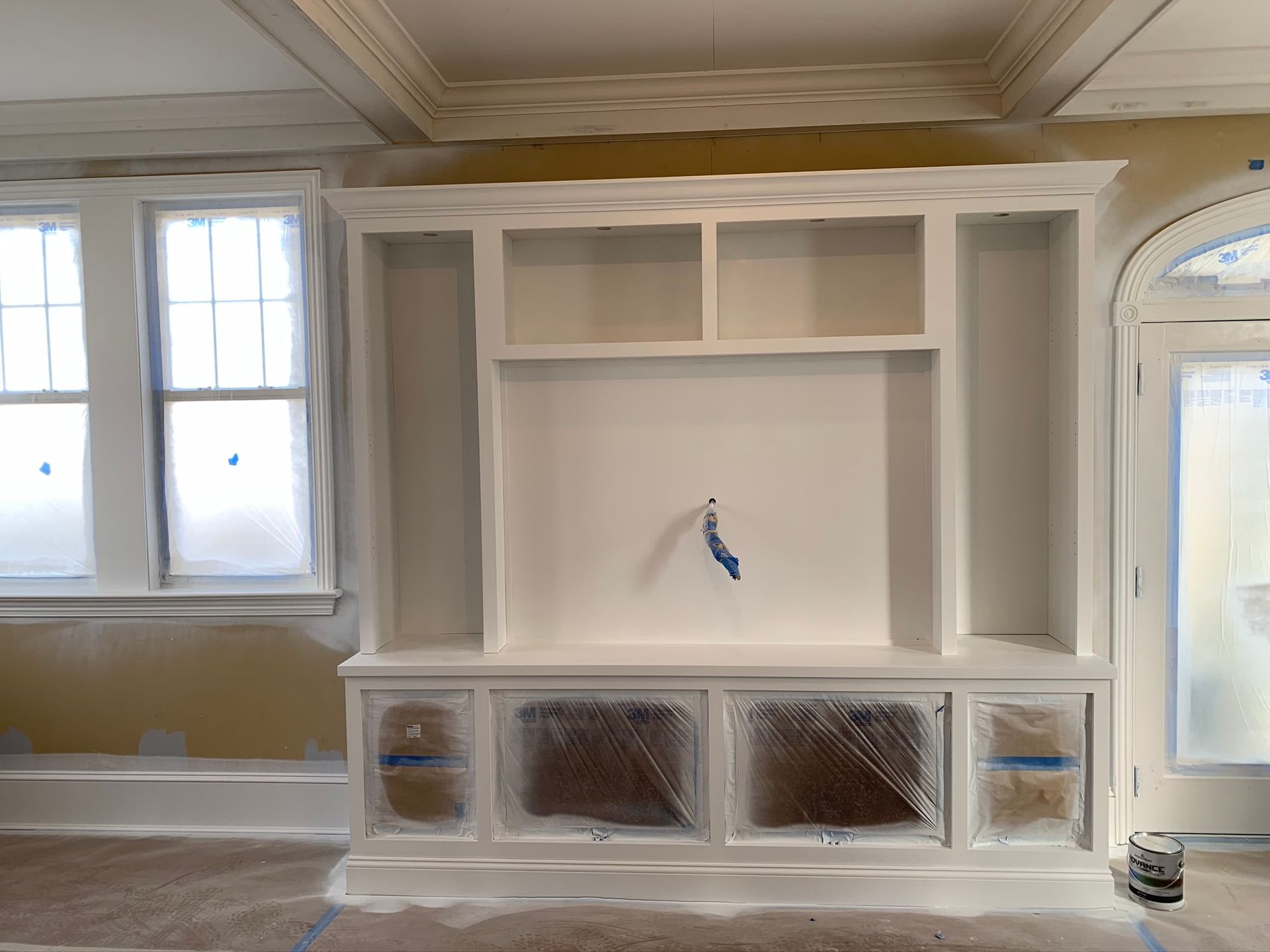 Built-in white cabinets and TV wall in a room under renovation, with plastic-covered lower panels.