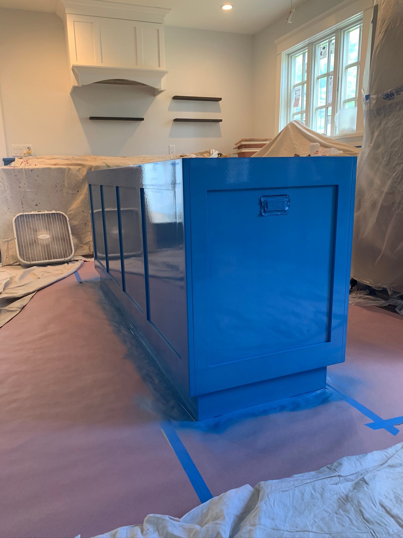 Kitchen island wrapped in blue protective film during renovation, with countertops and cabinets in a bright room