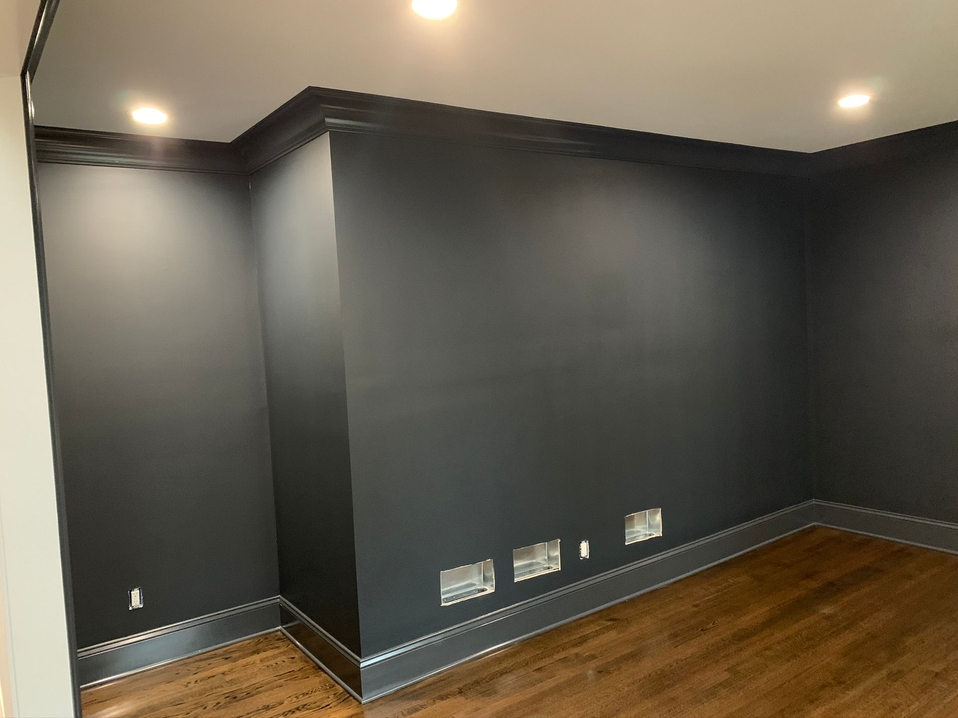 Empty room with dark gray walls, wood floor, and recessed ceiling lights