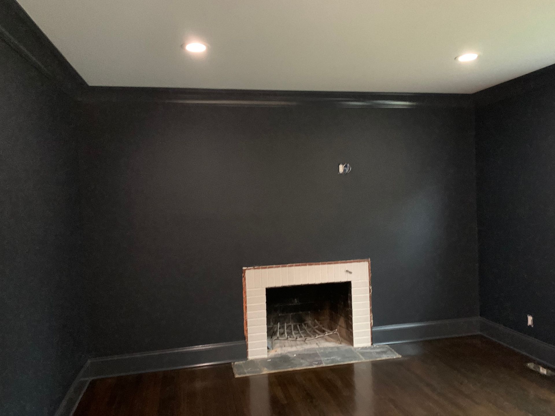 Empty room with dark walls, hardwood floor, and a small white fireplace centered on the far wall.