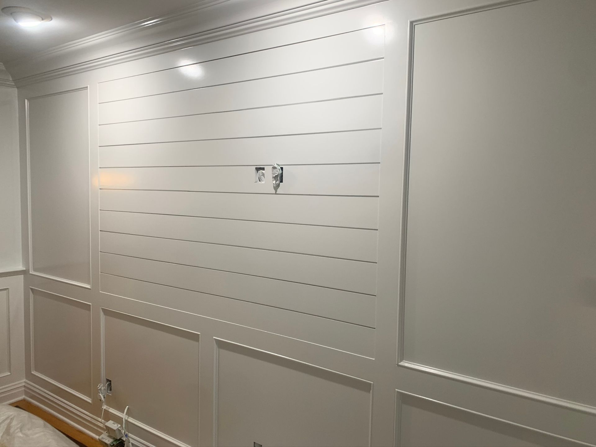 White paneled wall with decorative molding and a small wall-mounted fixture centered in the room.