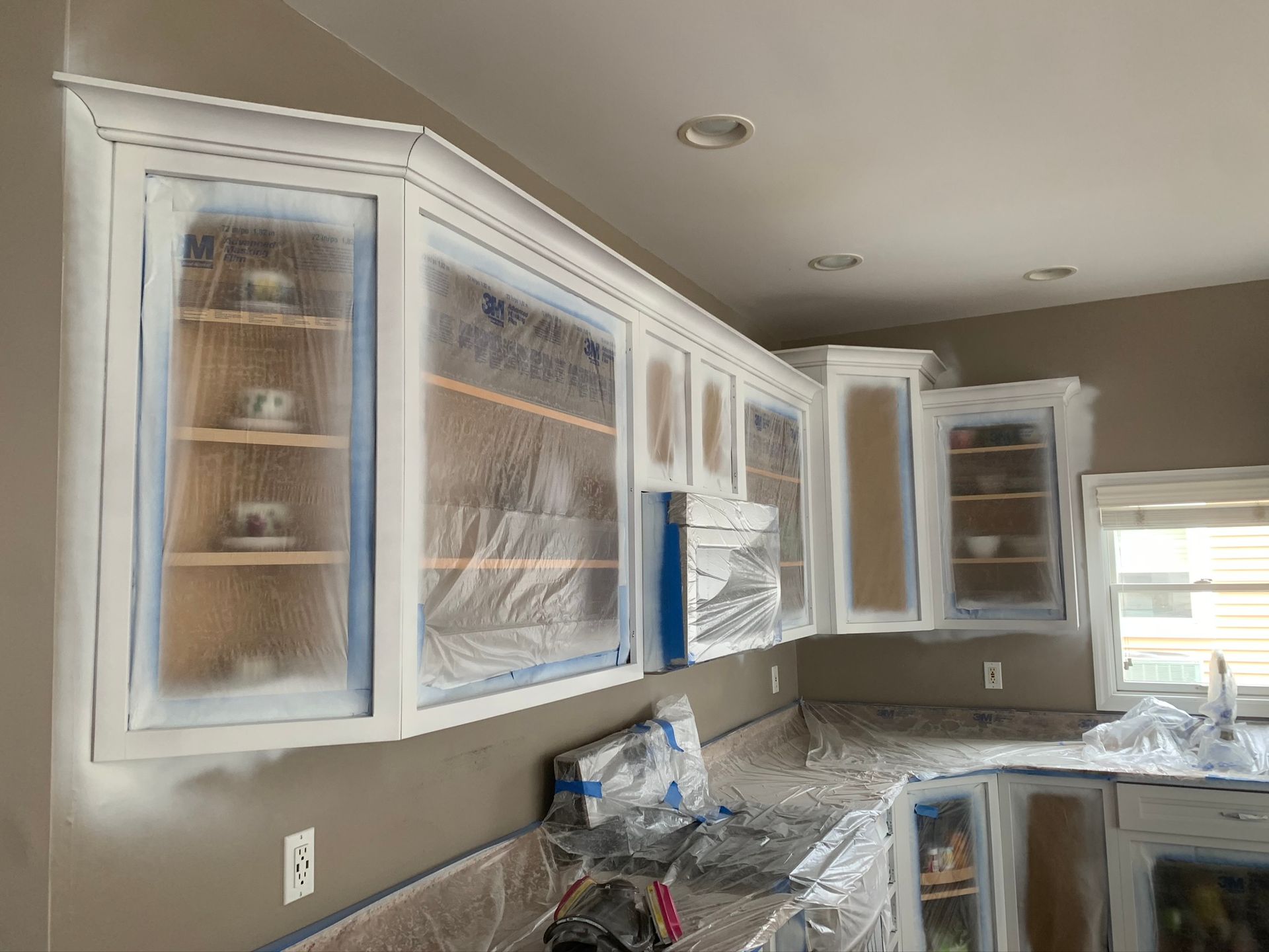 Kitchen with white cabinets covered in plastic, countertops cluttered during renovation.