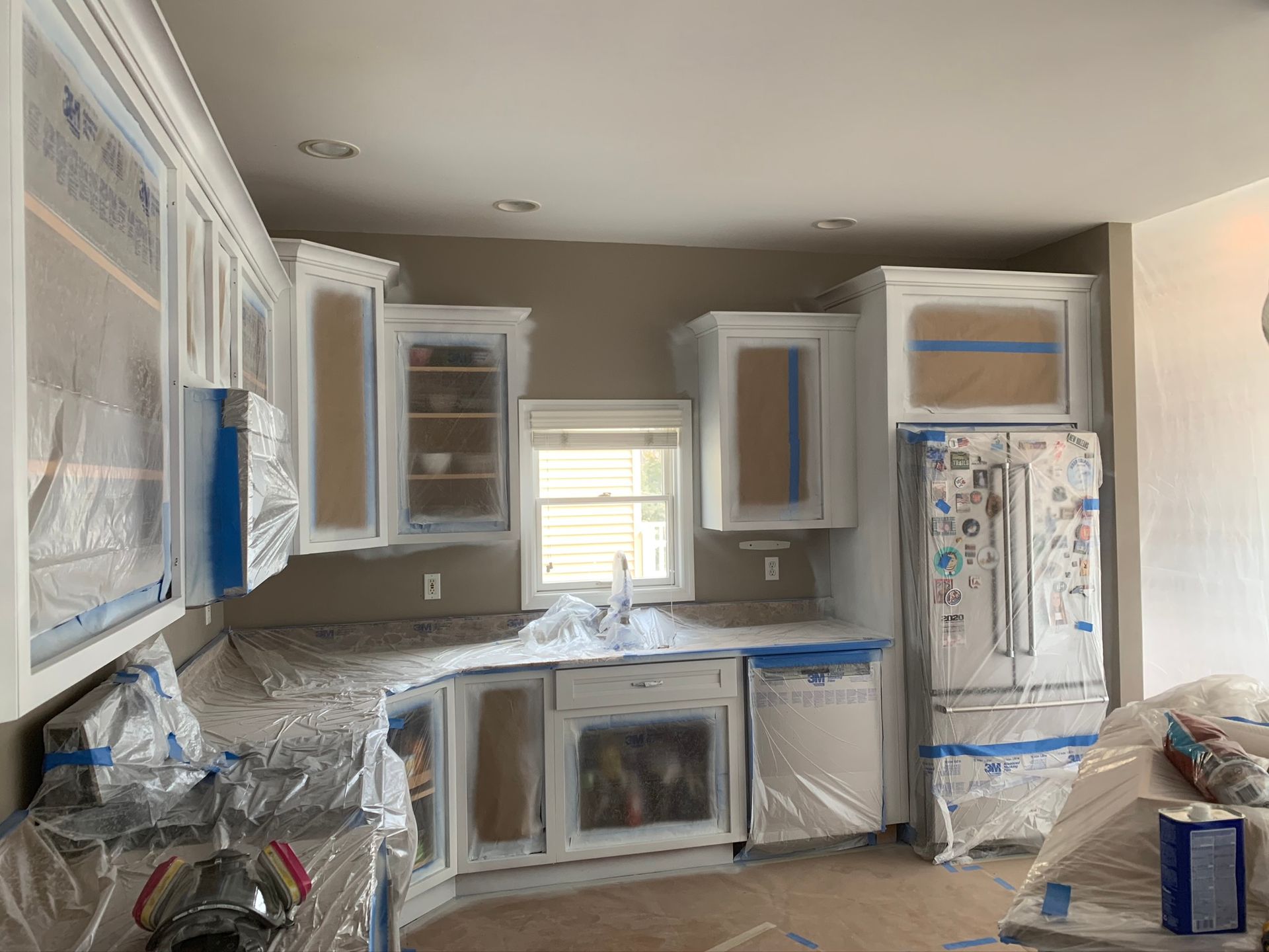 Kitchen under renovation with cabinets and appliances covered in plastic and painter’s tape
