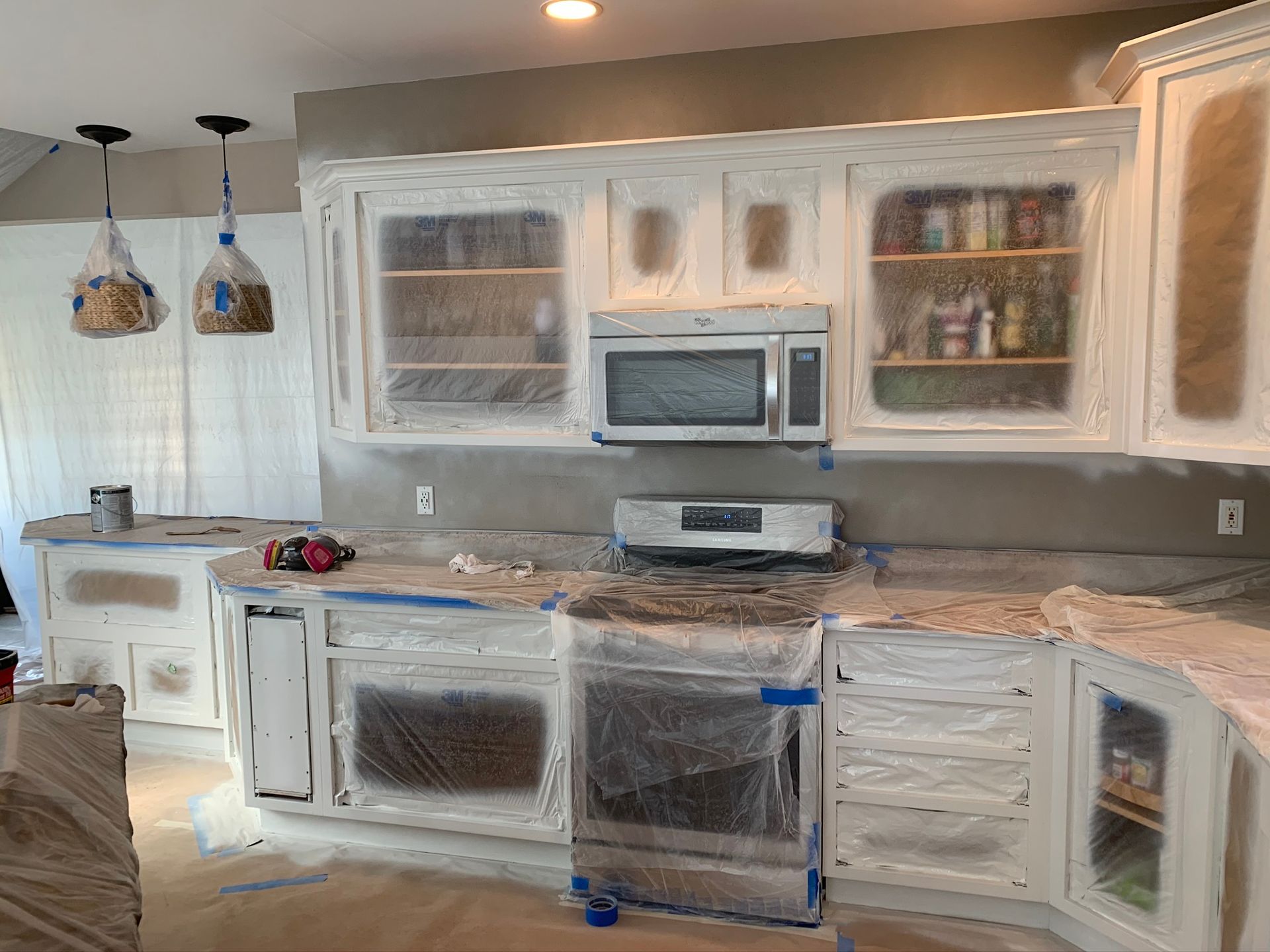 Kitchen under renovation with cabinets and counters covered in plastic sheeting, microwave installed in the center.