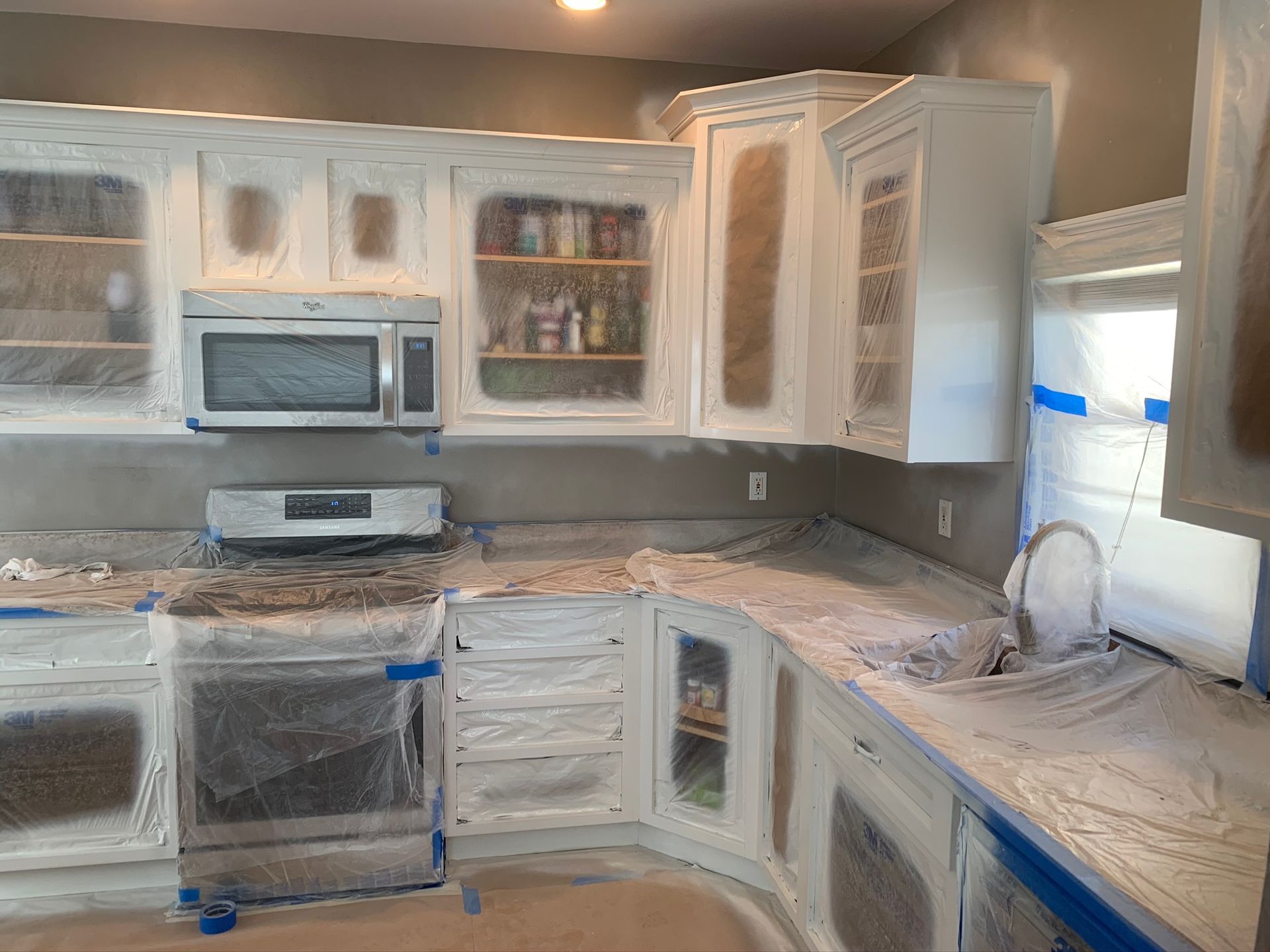 Freshly painted kitchen with white cabinets, granite countertops, and appliances under renovation
