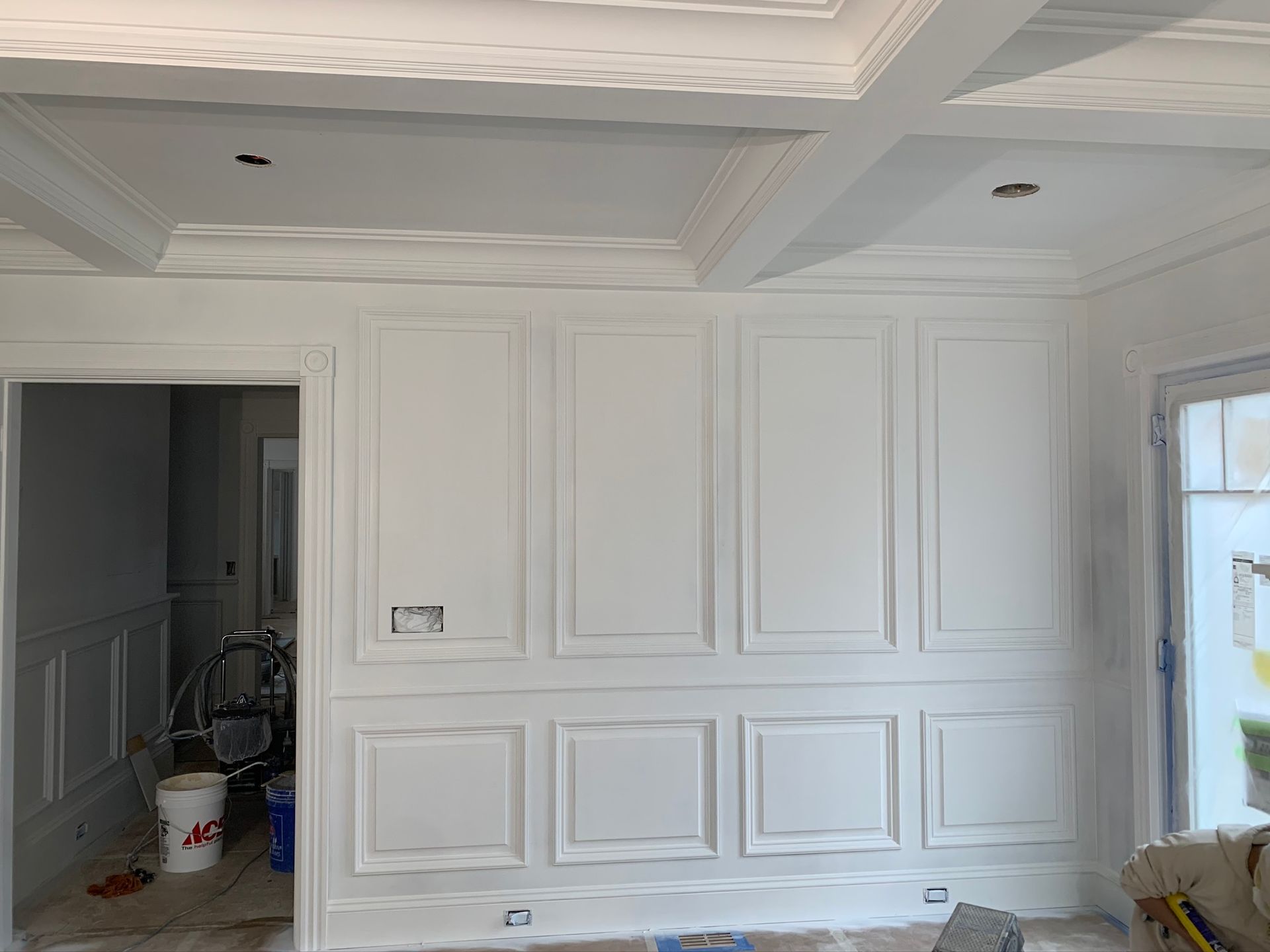 White paneled room with coffered ceiling, recessed lights, and a doorway leading to a cluttered adjoining room