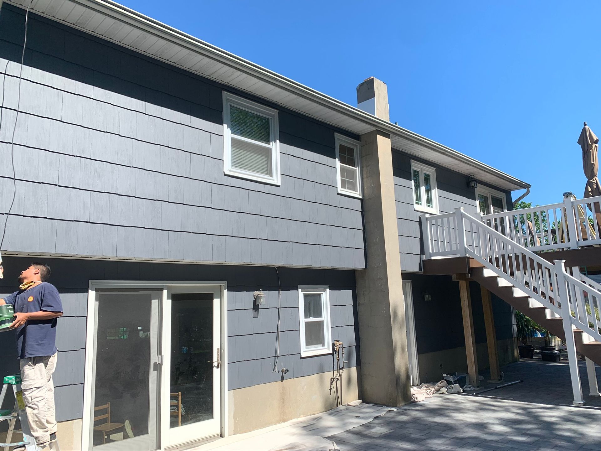 Exterior of a gray house with sliding glass doors, a deck, and an exterior staircase under a blue sky