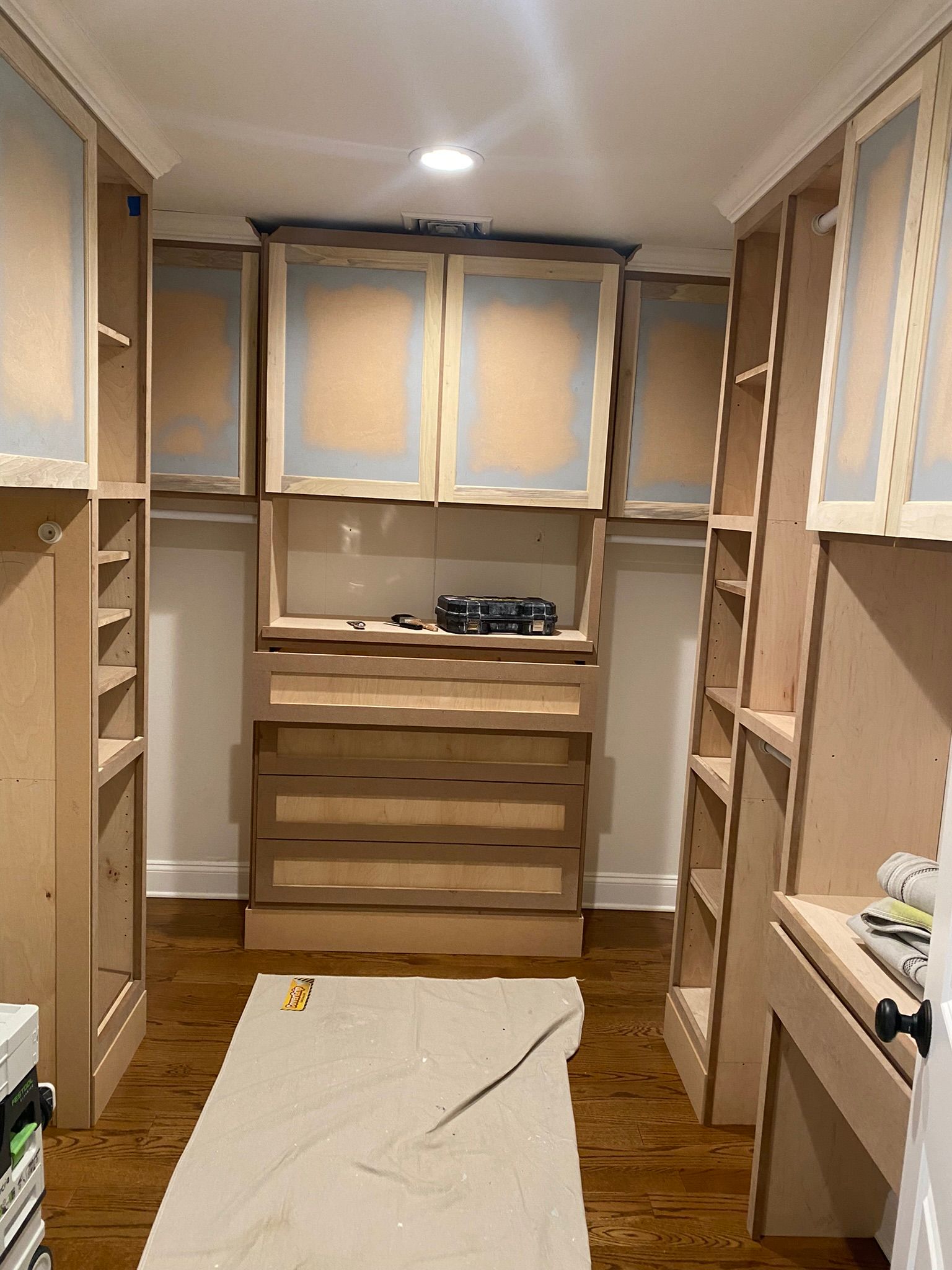 Unfinished walk-in closet with wood floors, built-in shelves, and cabinets under construction.