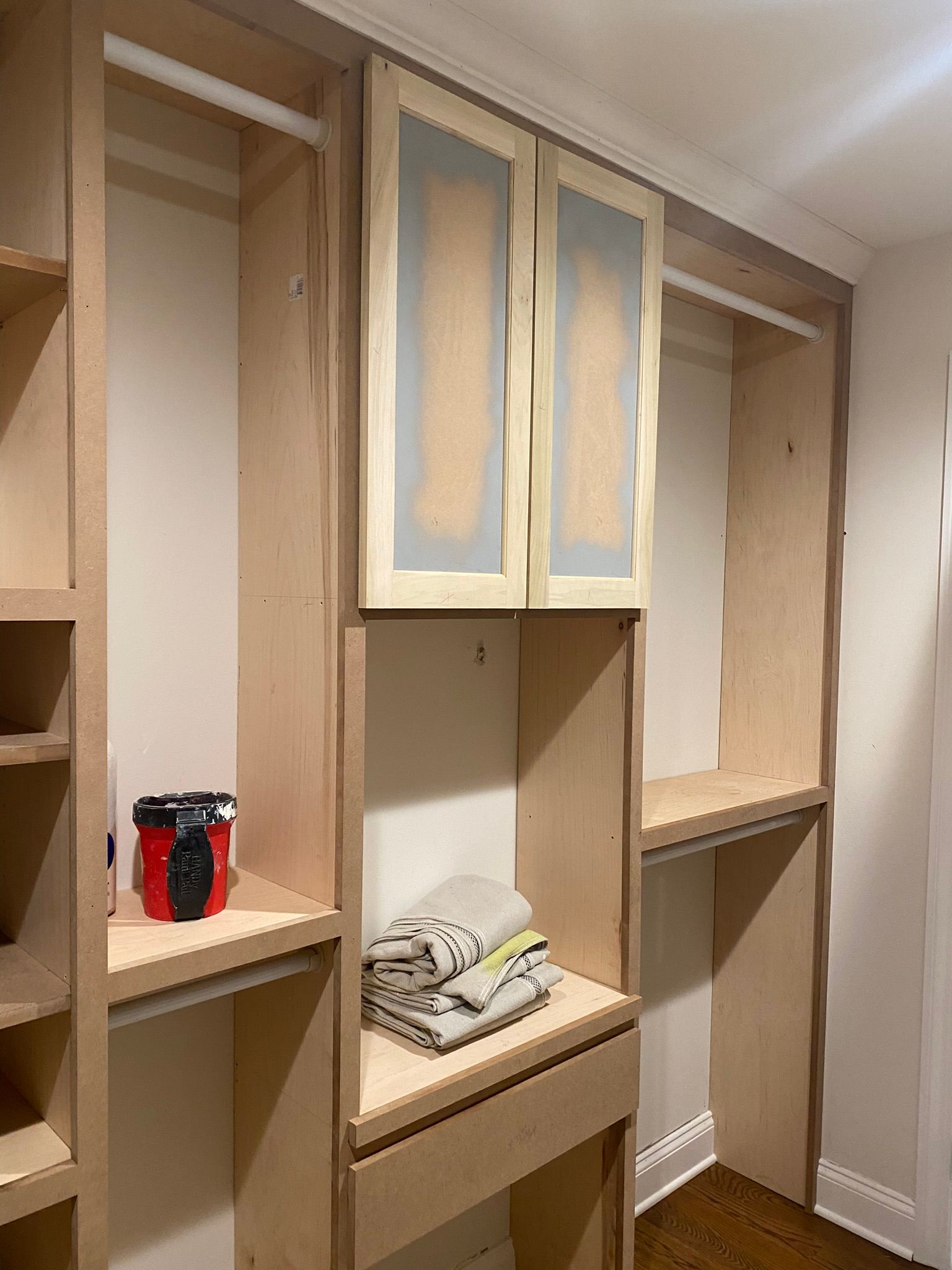 Built-in closet shelving with unfinished wood cabinets and open cubbies, one holding folded towels and bottles