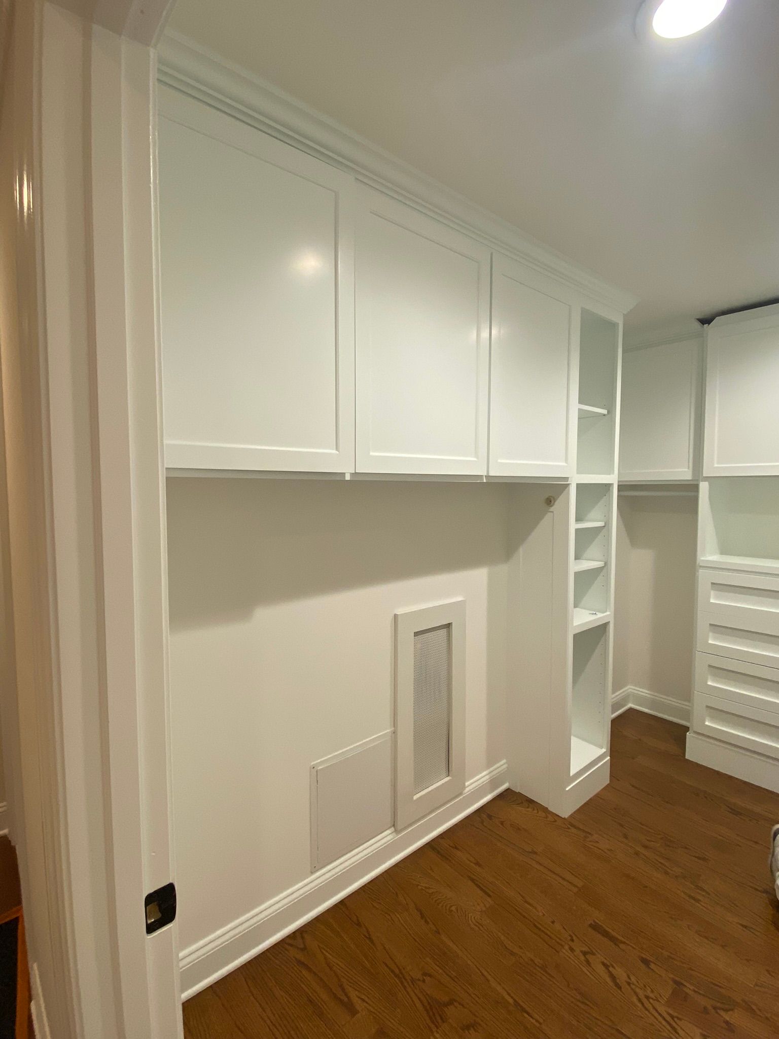 Built-in white cabinets and shelving in a walk-in closet with wood flooring and beige walls