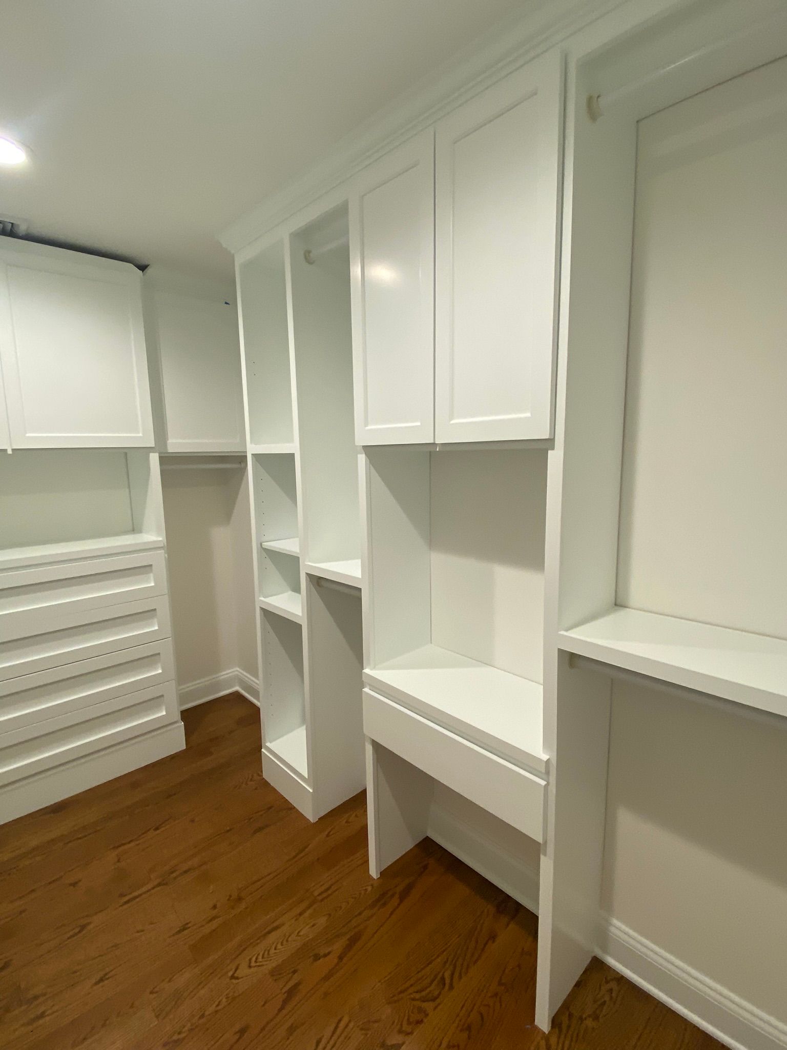 White built-in closet with shelves, drawers, and hanging sections in a wood-floored room.