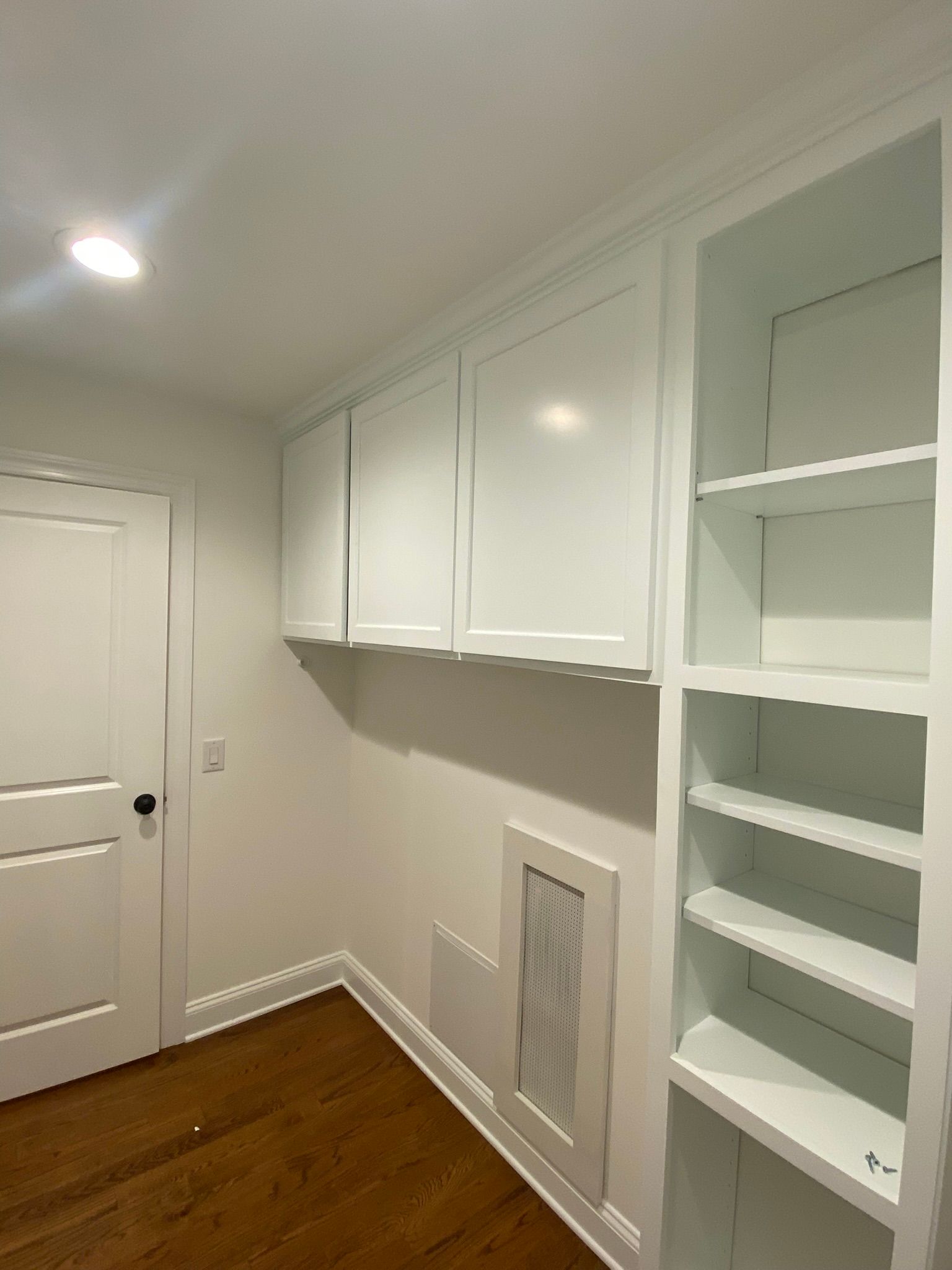 White built-in hallway cabinets and open shelves in a narrow room with hardwood floors.