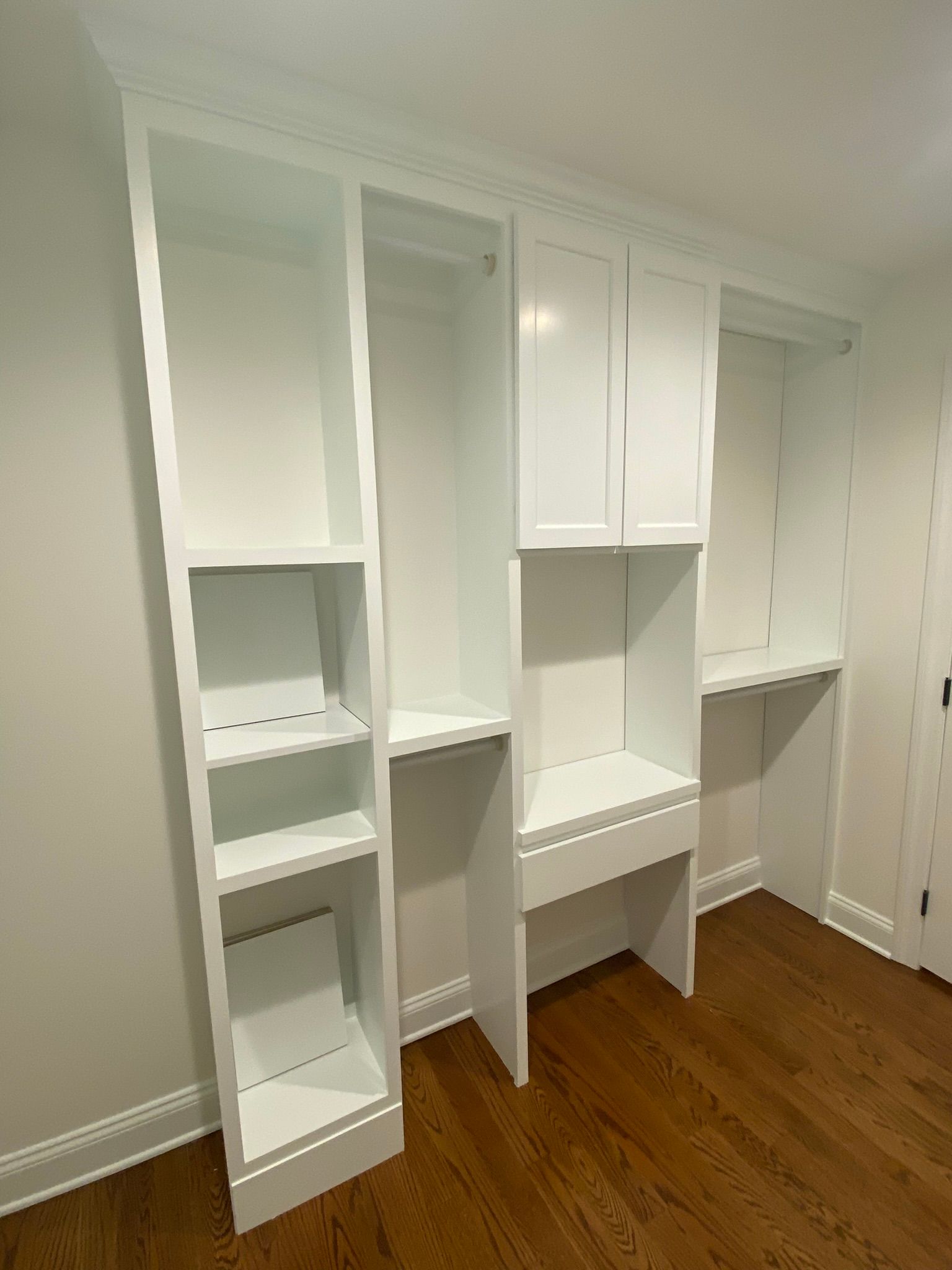 White built-in closet with shelves, cubbies, and a small desk alcove in a room with hardwood floor.