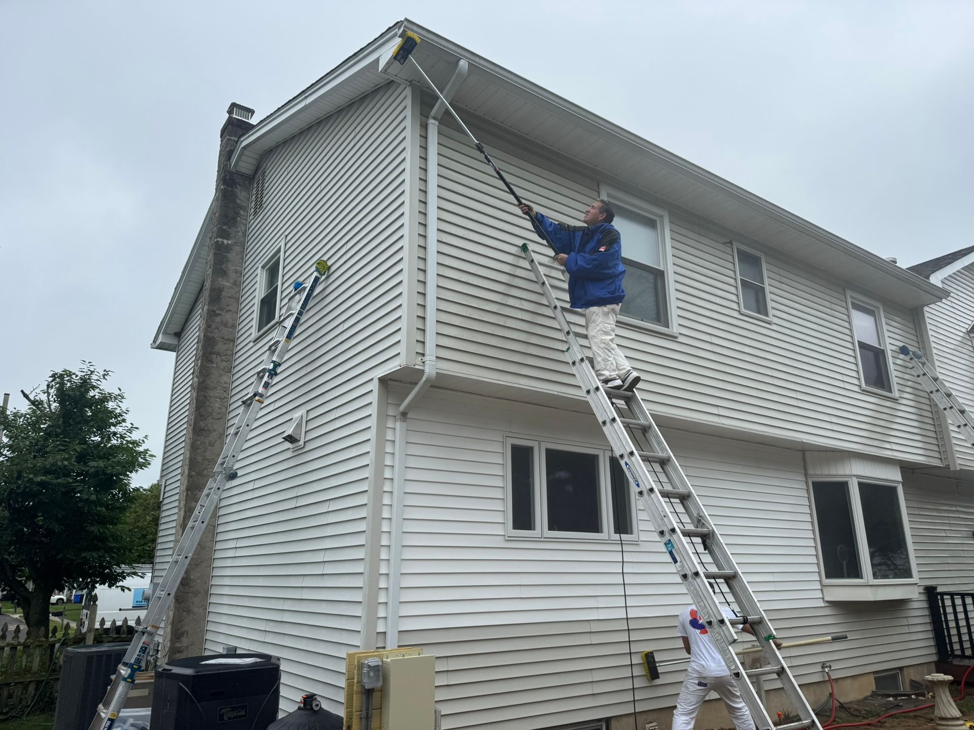 Worker on extension ladder painting the white siding of a two-story house