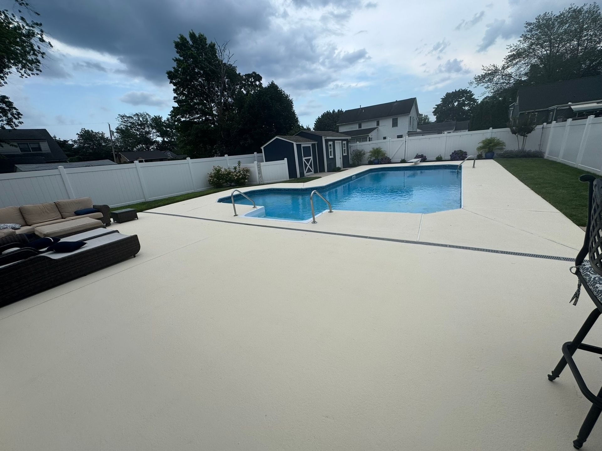 Backyard pool with white deck, lounge chairs, and cloudy sky
