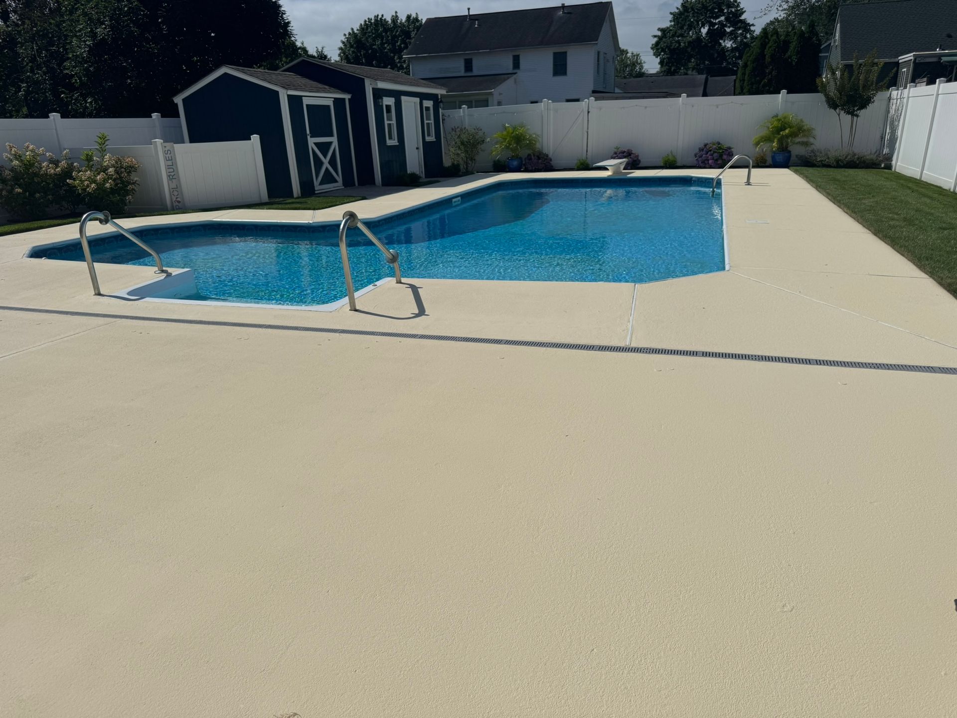 Backyard swimming pool with blue water, beige deck, and a small shed in the background.