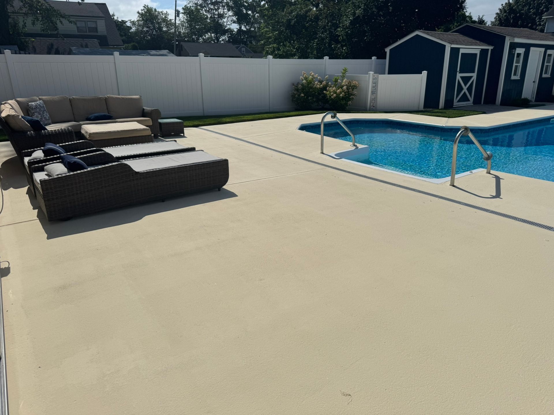 Backyard patio with lounge chairs, pool, and white privacy fence in bright sunlight