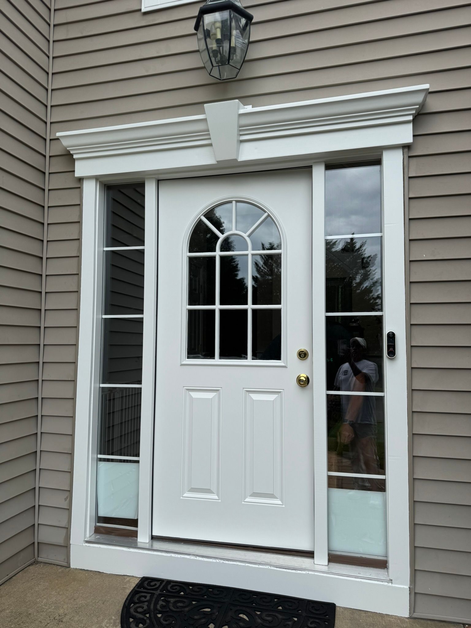 White front door with arched glass panels and sidelights under a porch light at a house entry