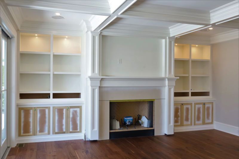 Built-in white shelving and cabinets flanking a central fireplace in a bright room with dark wood floors