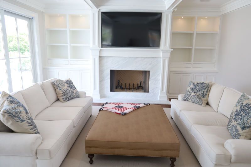 Bright living room with two cream sofas, wooden coffee table, fireplace, built-in shelves, and wall-mounted TV.