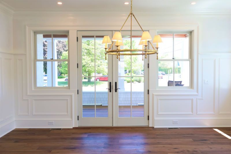 Bright empty dining room with white walls, French doors, chandelier, and dark wood floors