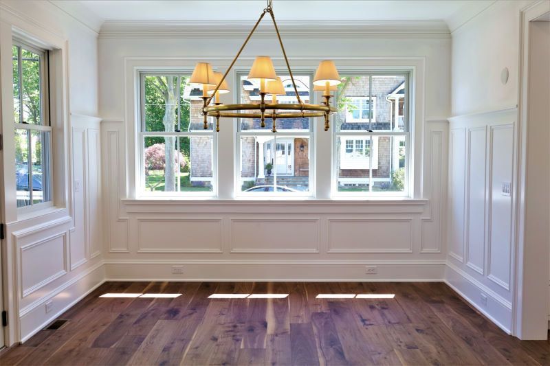 Empty dining room with dark wood floors, white wainscoting, and a chandelier in front of windows