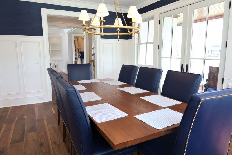 Formal dining room with a long wooden table, navy chairs, brass chandelier, and tall windows