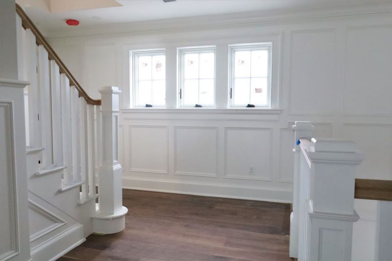 Bright white stairway landing with wood floor, paneled walls, and three windows above wainscoting.