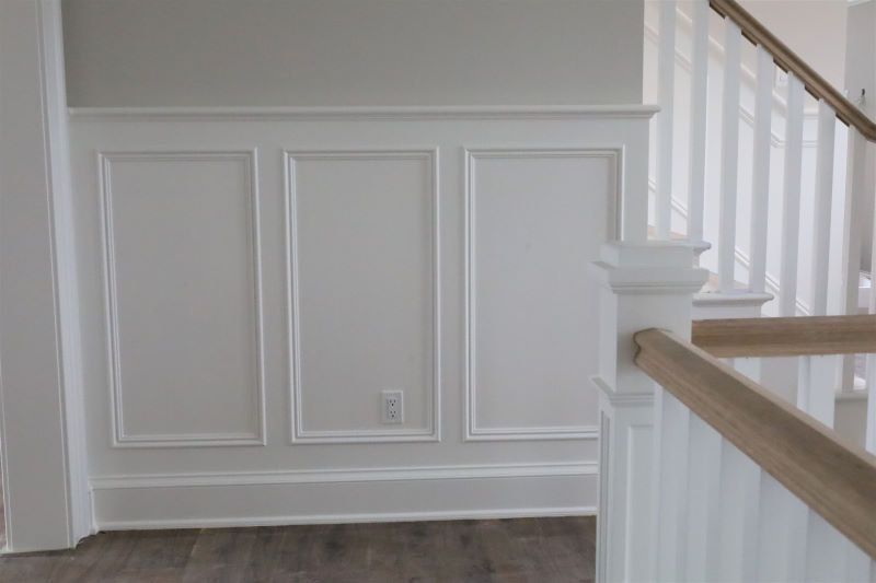 White paneled hallway wall with wainscoting, staircase railing, and wood floor