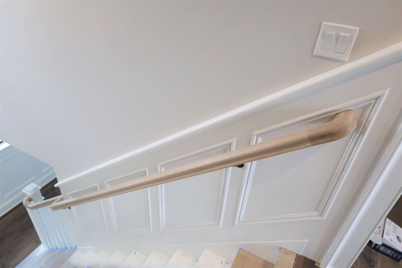 White stair railing with a wooden handrail beside a staircase in a bright interior hallway