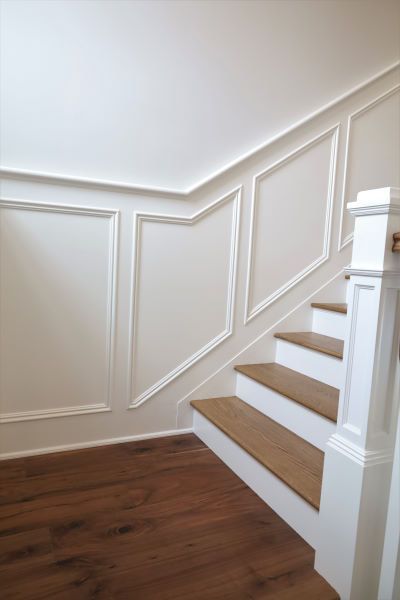 White staircase with wood treads and paneled walls in a bright interior.