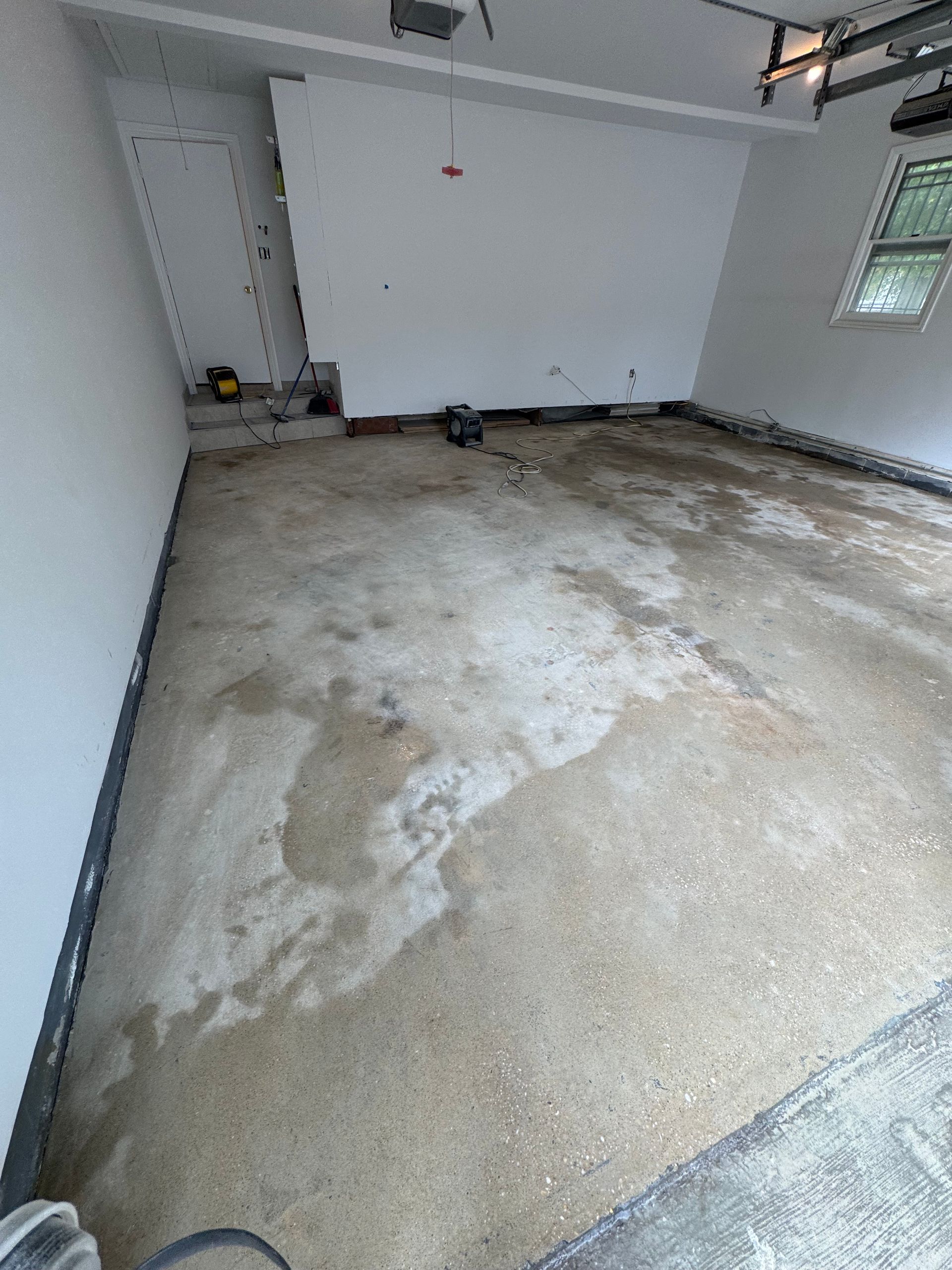 Empty garage with a stained concrete floor and white walls, viewed from the back toward the open entry.