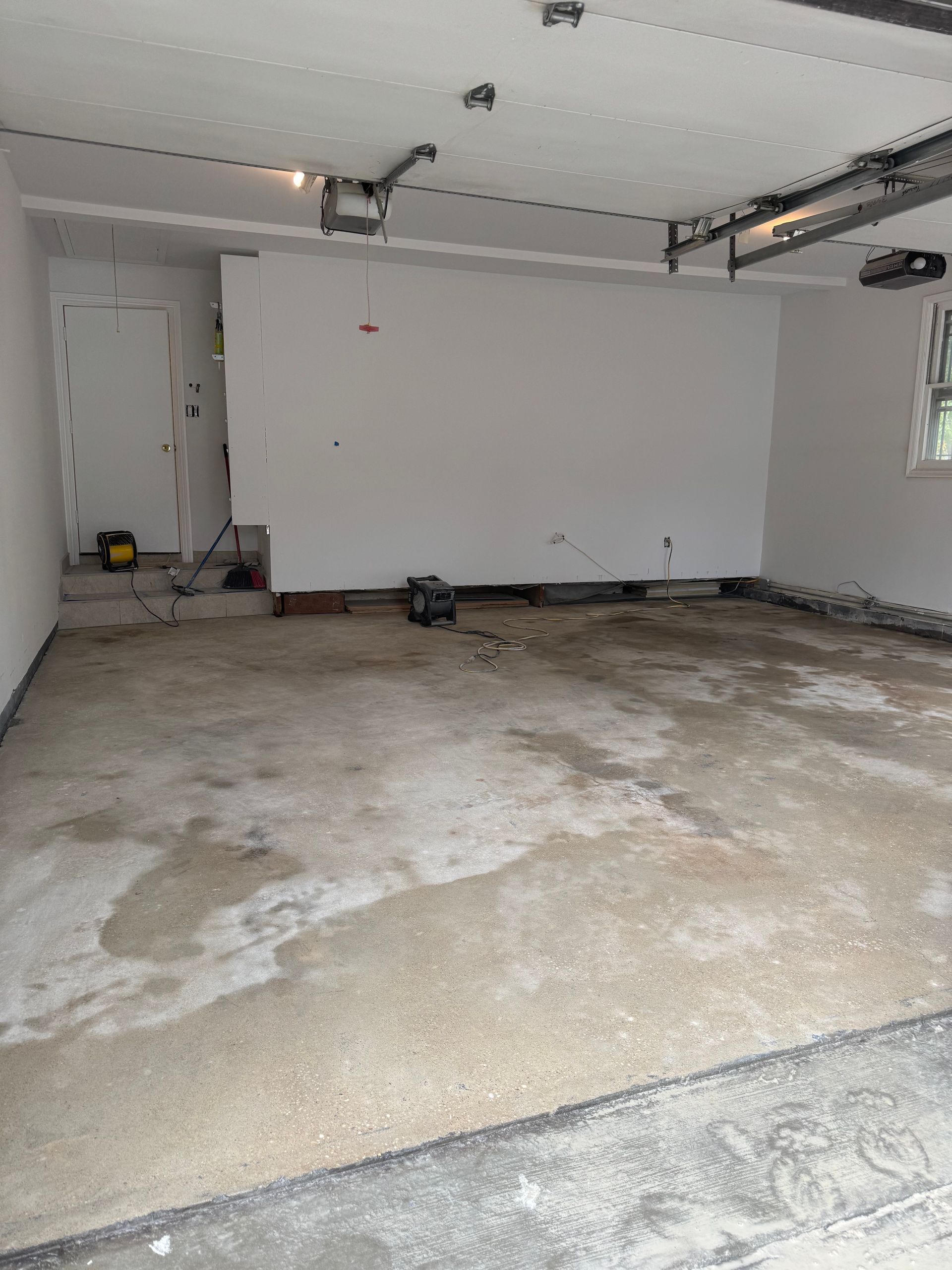 Empty residential garage with unfinished concrete floor, white walls, and closed garage door.