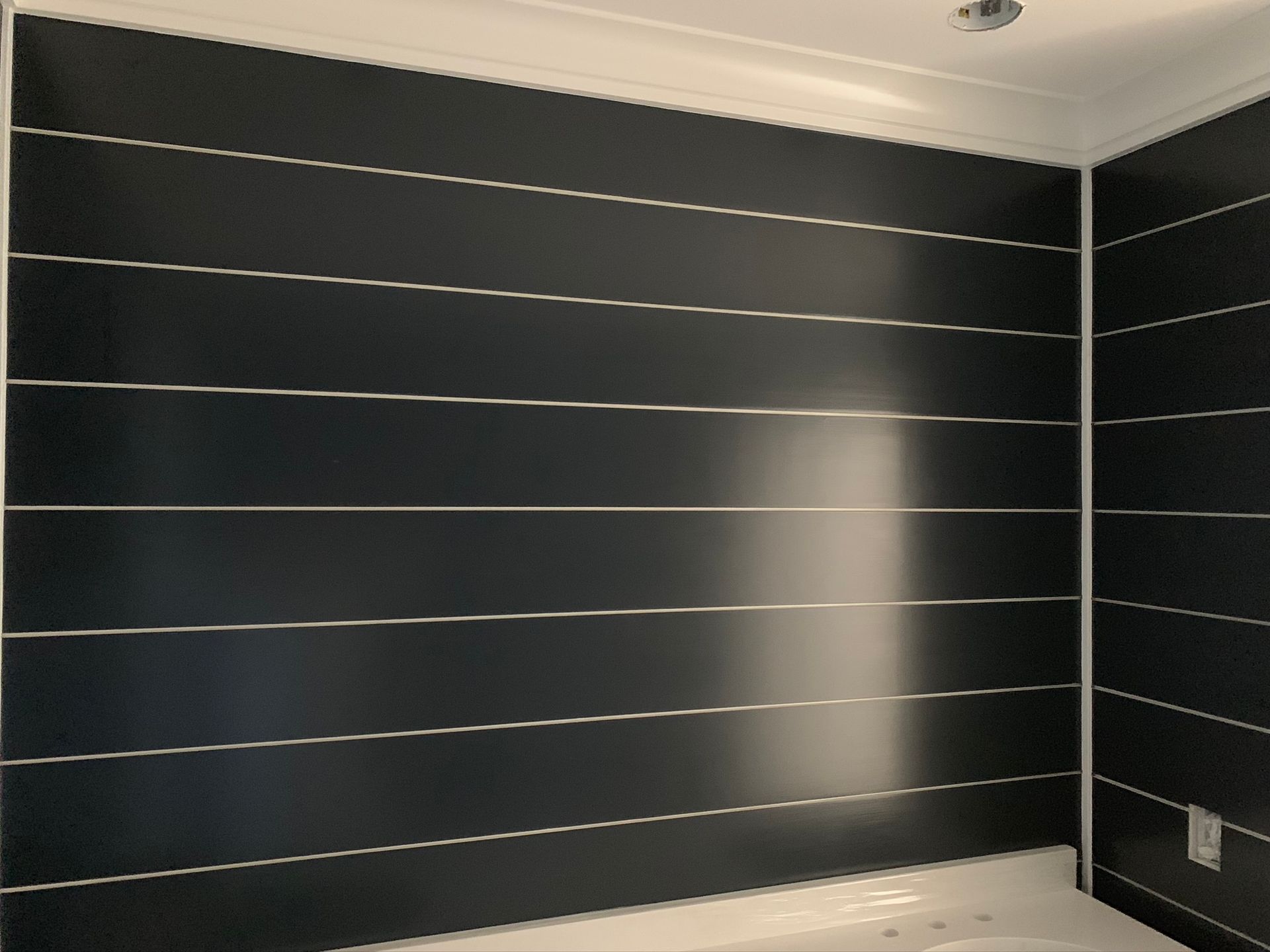 Empty room with dark gray slatted wall panels and white trim, softly lit from the right