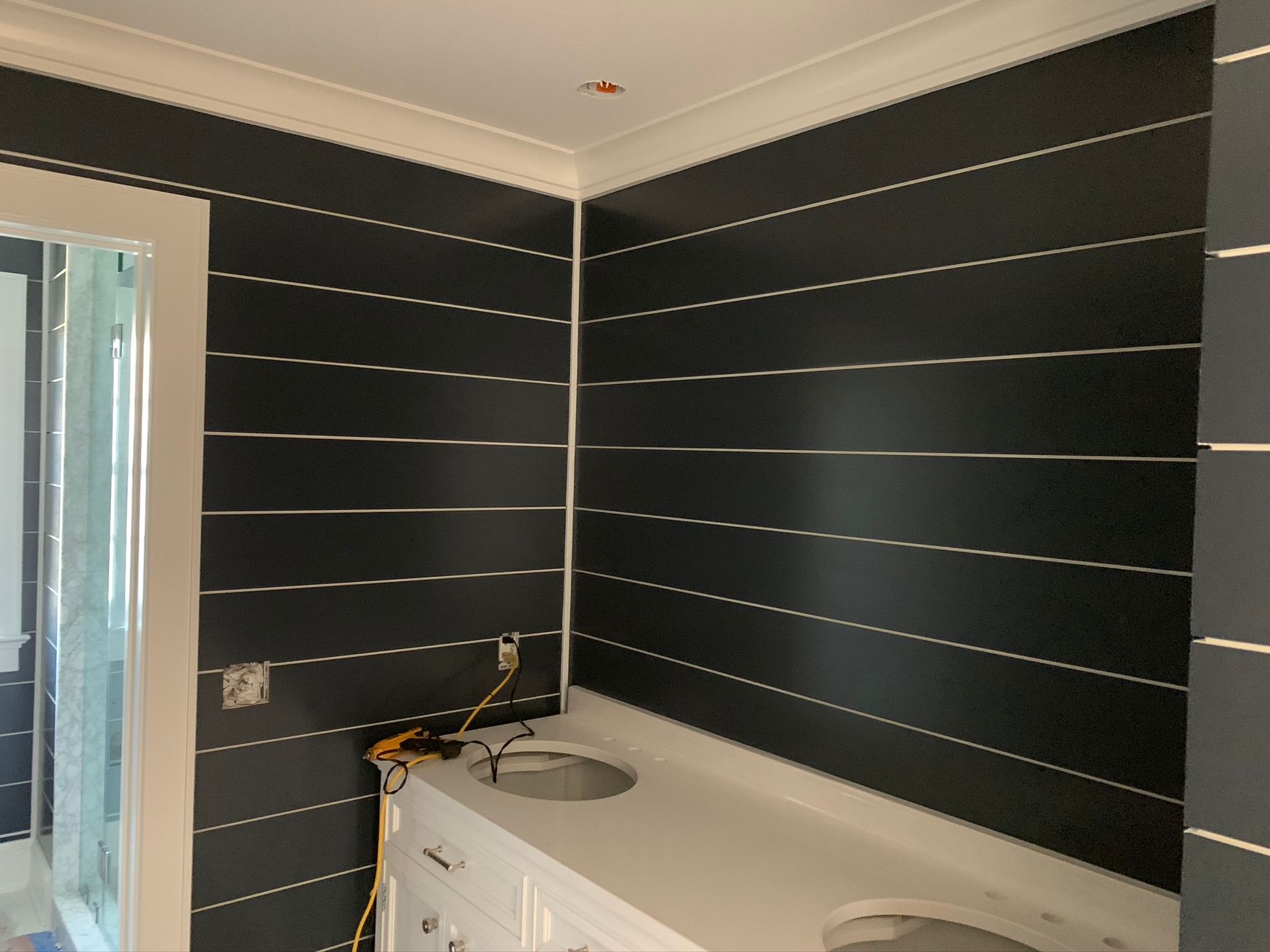 Modern bathroom with dark striped walls, white tub, and shower fixtures near a glass door