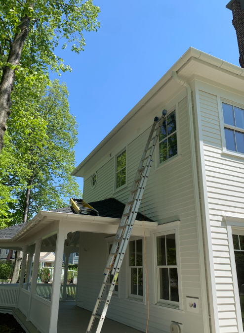 Ladder leaning against a white house’s second-story window under a bright blue sky