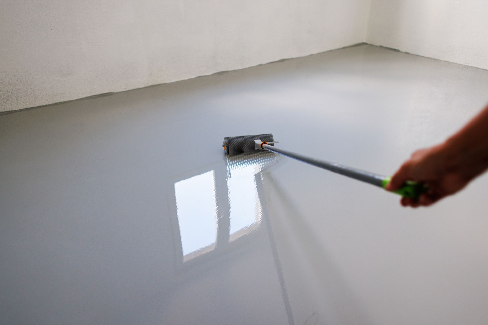 A person is painting a floor with a roller.