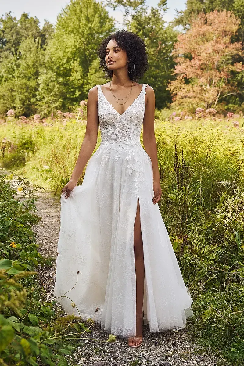 Woman in white wedding dress with a thigh-high slit, outdoors in a garden setting.