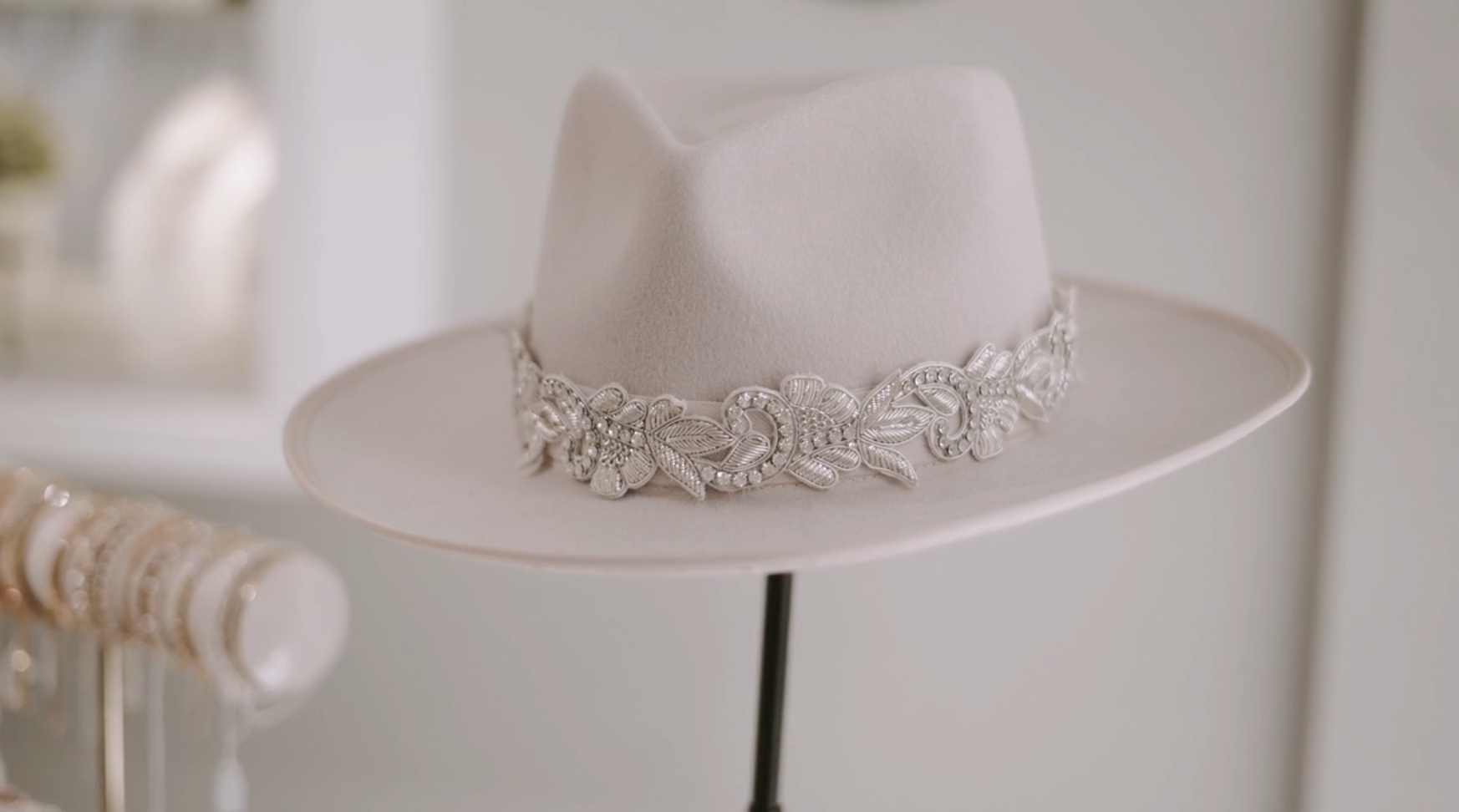 Light gray fedora hat with silver floral embellishment on a display stand.