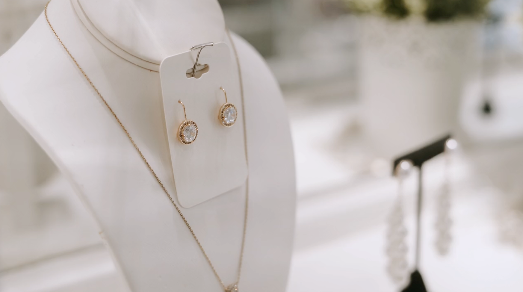 Jewelry display: gold necklace and earrings on a white mannequin, another earring stand in the background.