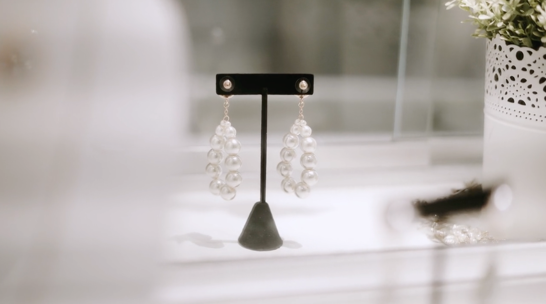 Pearl earrings displayed on a black jewelry stand, in a white setting.