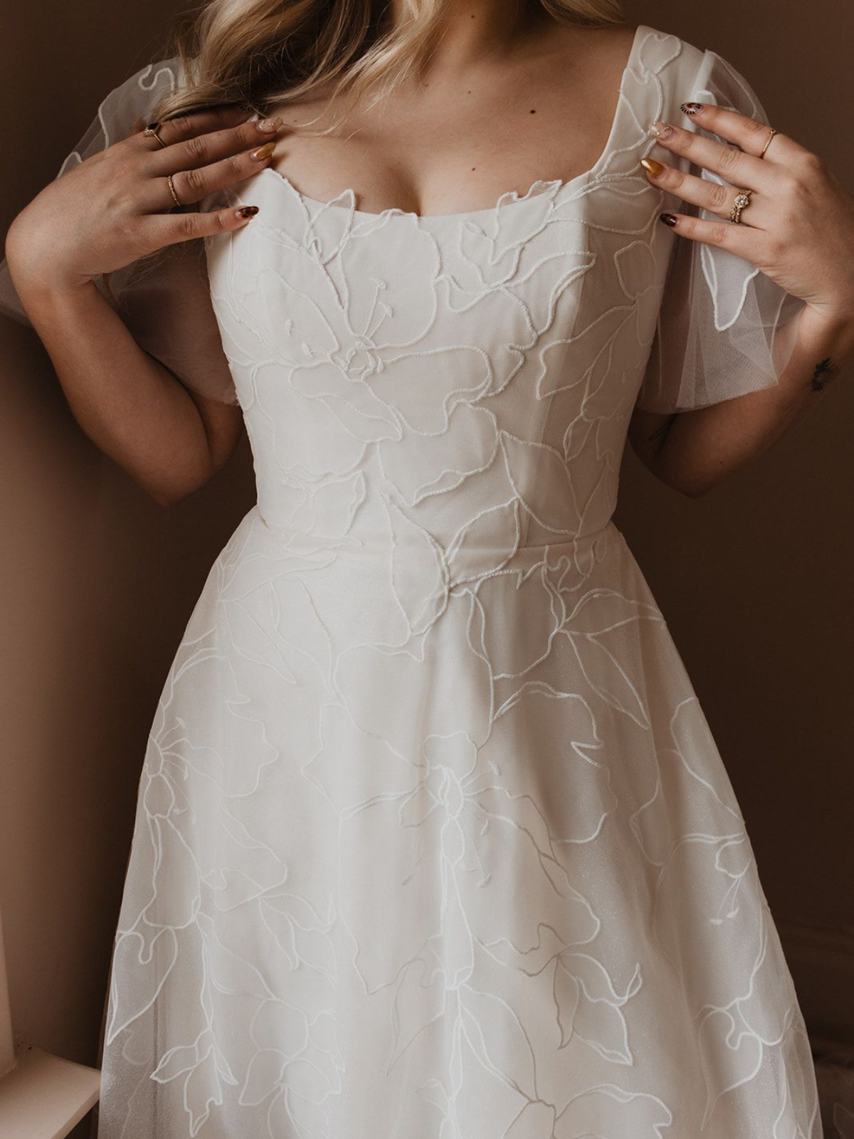 Woman in white lace dress, hands on chest. Beige background.