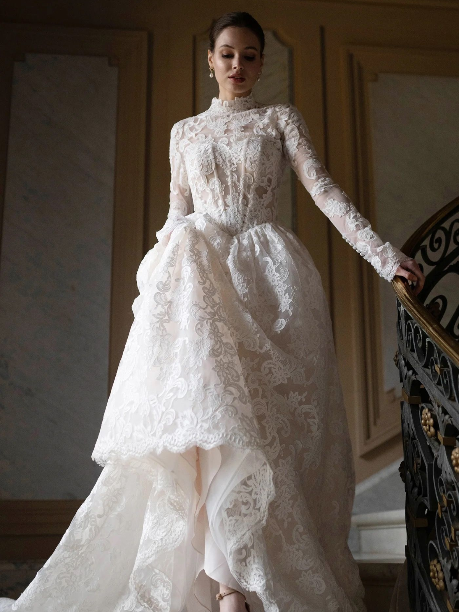 Woman in white lace gown on ornate staircase.