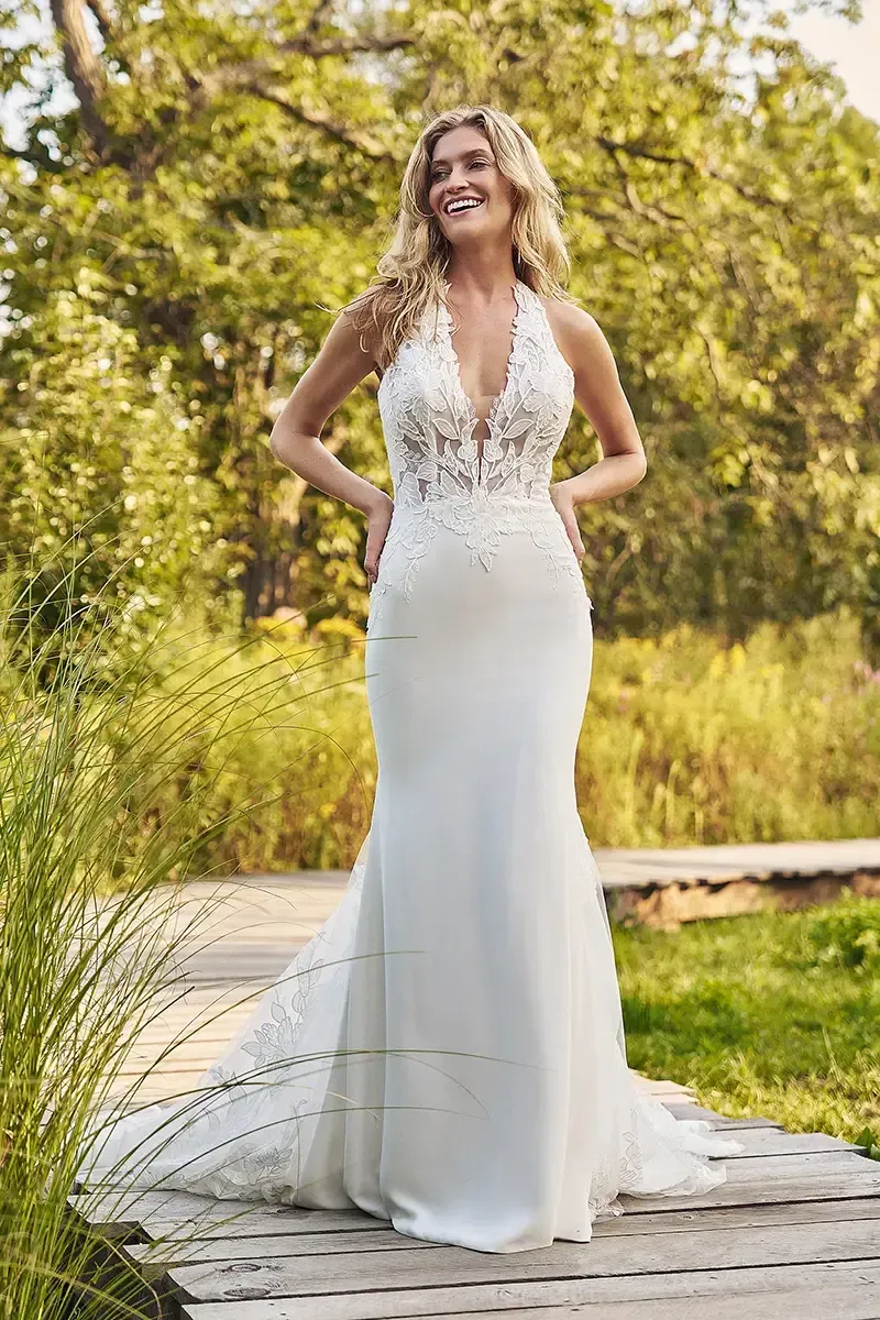 Woman in a white wedding dress with a train, outdoors, smiling.