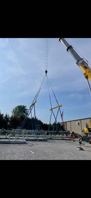 Crane lifting a large metal frame at a construction site with workers nearby under a blue sky