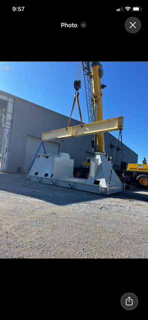 Yellow crane lifting a large metal beam beside a white industrial building under a blue sky