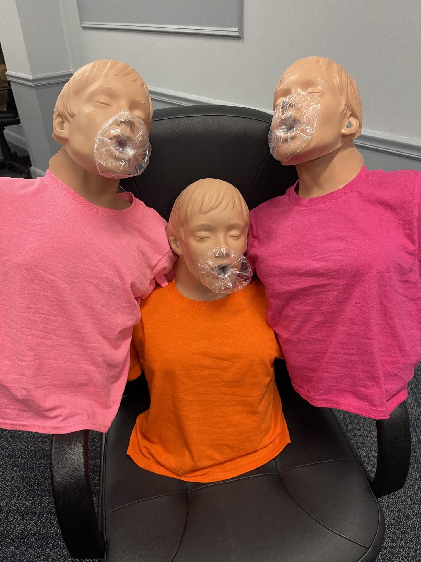 Three mannequin heads and torsos in pink and orange shirts on a black chair indoors