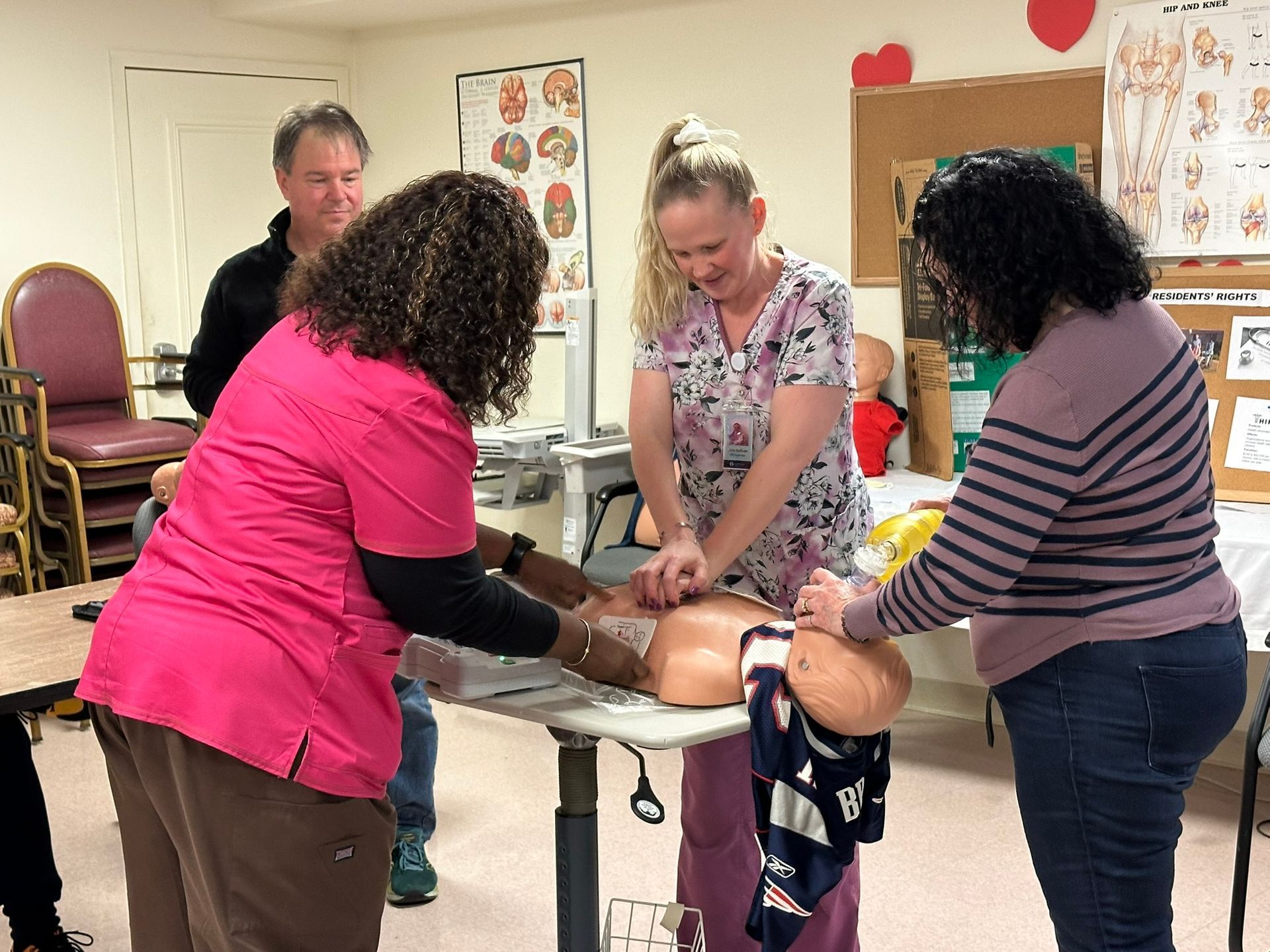 People practicing CPR on a training manikin in a classroom setting.
